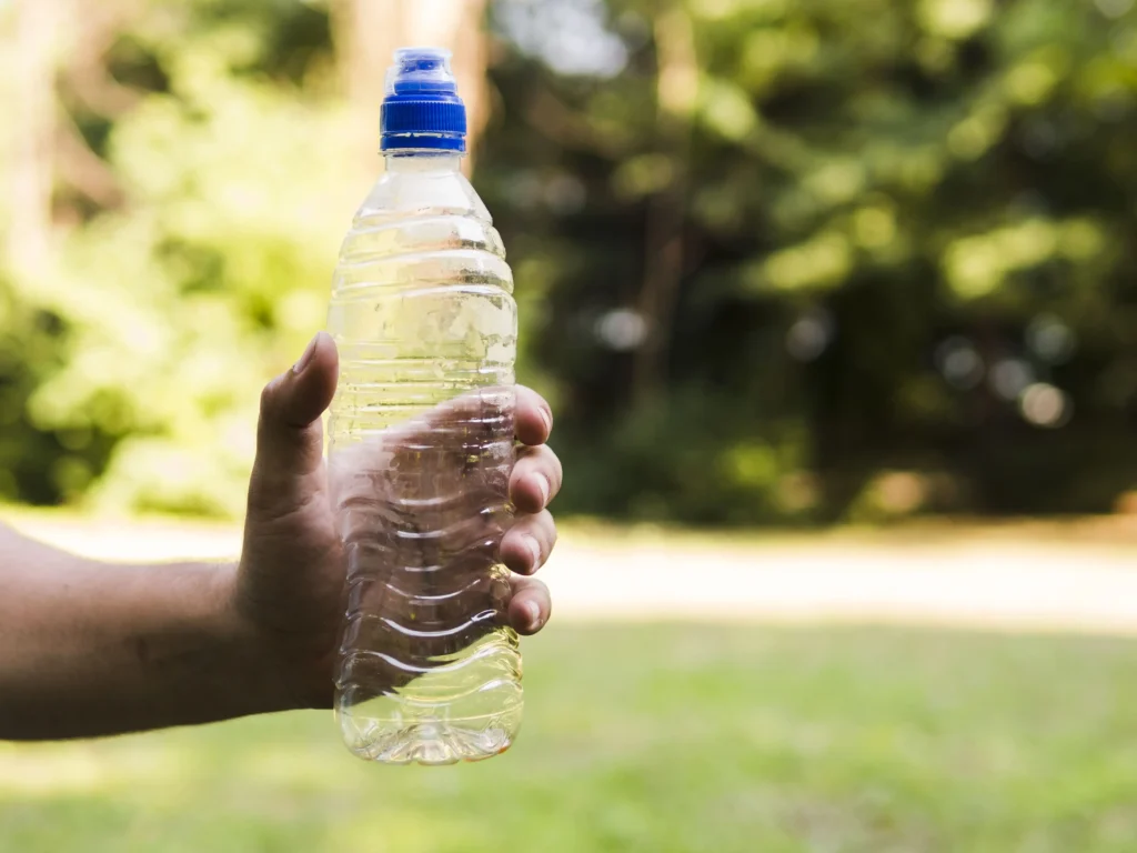 man s hand holding empty plastic water bottle outdoors