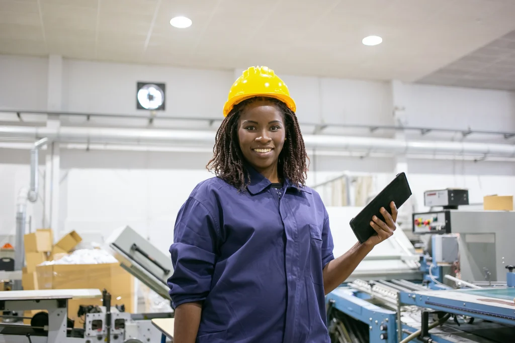 Manpower Outsourcing: Benefits, Risks and Considerations happy female factory worker hardhat overall standing machine holding tablet looking front smiling